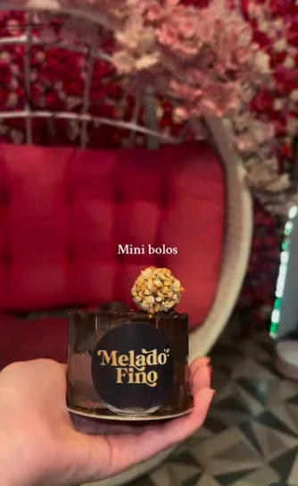 Mini bolo de chocolate com o selo da Melado Fino, na frente do balanço de flores da loja